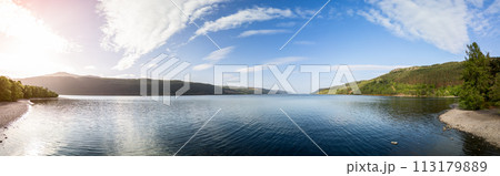 Panoramic drone view of Loch Ness, sun rays warming tranquil waters and pebbled shores 113179889