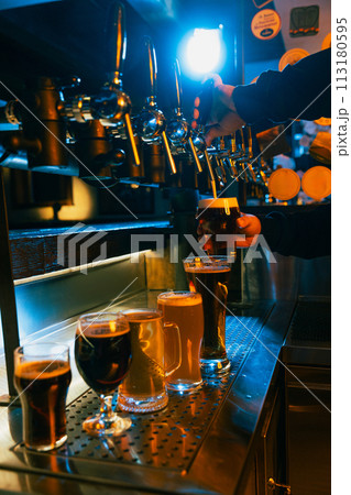 Craft beer tap pouring frothy beverage with range of filled light and dark beer, ale glasses in front. Serving craft beer from tap. 113180595