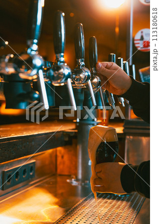 Craft, lager, cold, foamy dark beer poured into stemmed glass by bartender at traditional bar. Serving craft beer from tap. Concept of Oktoberfest. Craft, lager, cold, foamy dark beer poured into stemmed glass by bartender at traditional bar. Serving craft beer from tap. Concept of Oktoberfest. 113180618