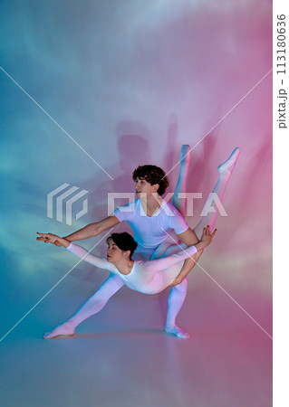 Ballet duo performing acrobatic figure, male supporting female in aerial split pose against gradient studio background. 113180636