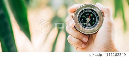 A traveler holding a compass in a park searches for guidance and direction amidst nature beauty. The compass in the woman hand signifies exploration and a journey to find her path. 113182249