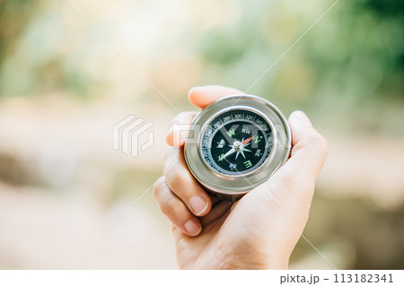 A traveler holding a compass in a park seeking guidance and direction. The compass in the woman hand against a nature-blurred background signifies exploration and a journey to find one way. A traveler holding a compass in a park seeking guidance and direction. The compass in the woman hand against a nature-blurred background signifies exploration and a journey to find one way. 113182341