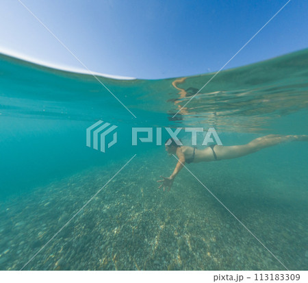 Sea summer landscape. Travel and Holiday concept. A brunette woman diving into blue sea water. Underwater photography of sport activity Sea summer landscape. Travel and Holiday concept. A brunette woman diving into blue sea water. Underwater photography of sport activity 113183309