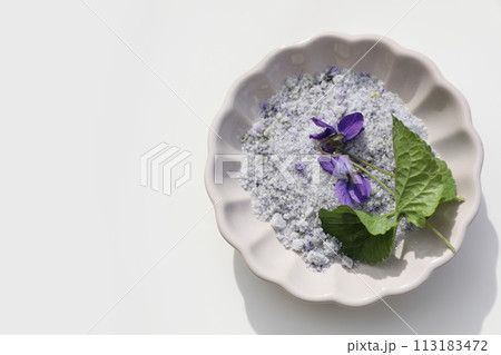 Homemade herbal sugar decorated by violet flowers and leaves. Scalloped ceramic plate isolated on white background. Viola odorata. Fragrant natural cough remedy. Food flat lay, top view. Bath salt. Homemade herbal sugar decorated by violet flowers and leaves. Scalloped ceramic plate isolated on white background. Viola odorata. Fragrant natural cough remedy. Food flat lay, top view. Bath salt. 113183472