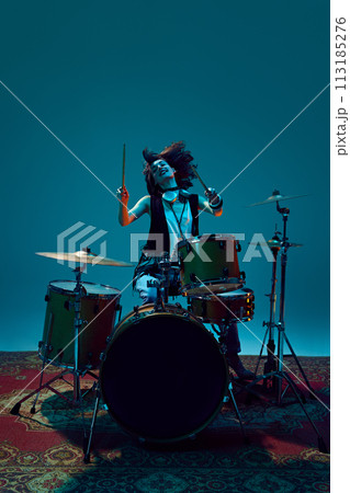 Artistic, expressive young woman, musician playing drums against cyan background in neon light 113185276