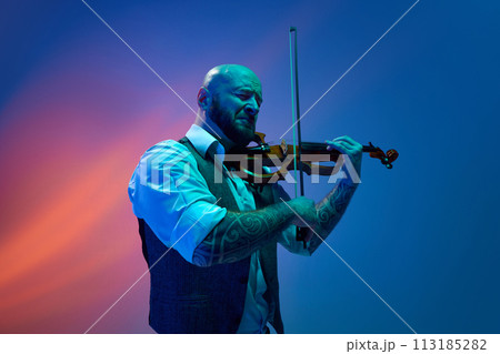 Deep feelings of melody. Young bald man playing violin against blue background in neon with mixed light 113185282