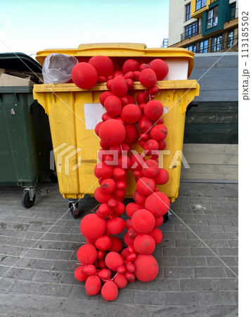 Red balloon garlands in a dumpster. Discarded used decoration. Concept of the melancholy after holiday party 113185502