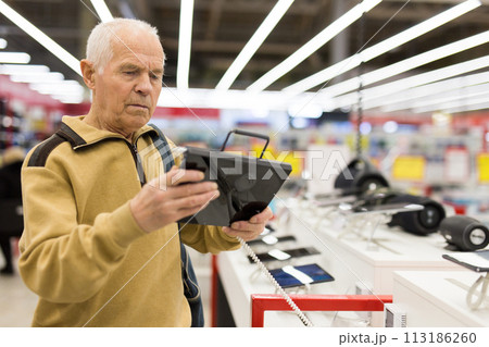 elderly man examines tablet computer in showroom of electronics store 113186260