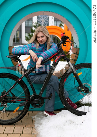 Lifestyle concept. A woman in a blue jacket took a break while riding a bicycle at the playground Lifestyle concept. A woman in a blue jacket took a break while riding a bicycle at the playground 113186473