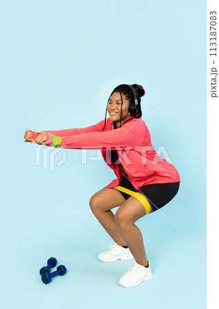 A Young Woman Squatting with a Fitness Band and Headphones A Young Woman Squatting with a Fitness Band and Headphones 113187083