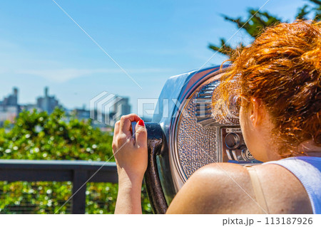 Young cute woman looking at skyline through Coin operated binoculars 113187926