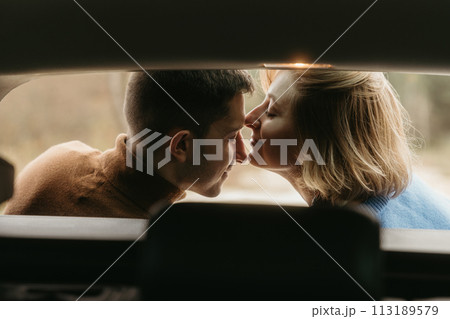 Intimate moment woman and man sitting in the open trunk of a car while traveling in autumn and kissing Intimate moment woman and man sitting in the open trunk of a car while traveling in autumn and kissing 113189579