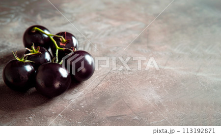 black purple cherry tomatoes closeup on gray stone background Gardening and harvesting Healthy food copy space 113192871