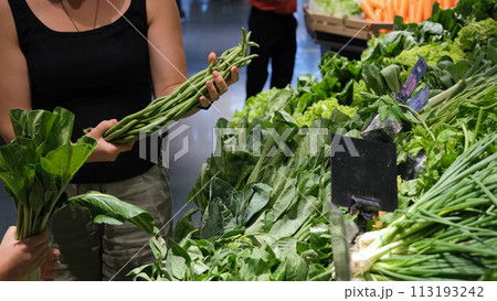 Young woman with little daughter buying fresh herbs at grocery. Choosing long beans, bunching onion and spinach Young woman with little daughter buying fresh herbs at grocery. Choosing long beans, bunching onion and spinach 113193242