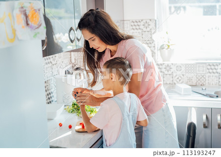 Caring young Mother putting a plaster on child finger with wound on from a cut by kitchen knife. First aid in case of small domestic injury. Children's injuries at home. Negligence in cooking at home. 113193247