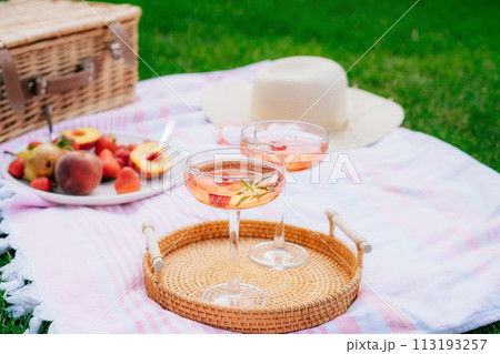 Pink drinks, cocktail with ice, raspberry, rosemary. Two glasses with martini, champagne, cider, lemonade on the blanket with fruit plate, picnic basket, Cozy summer picnic on nature. Selective focus. 113193257
