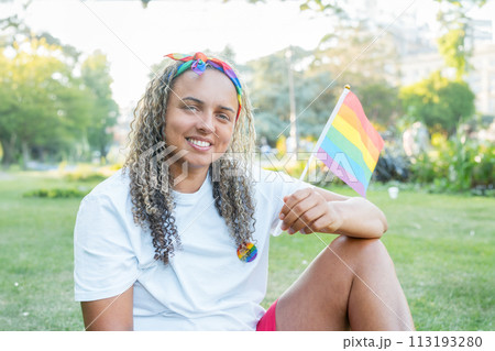 Mixed race woman with small rainbow flag outdoor. Young lesbian activist smiling and holding flag symbol of social movement Lgbtq. Fight for equality, freedom and human rights. Celebrating Pride month Mixed race woman with small rainbow flag outdoor. Young lesbian activist smiling and holding flag symbol of social movement Lgbtq. Fight for equality, freedom and human rights. Celebrating Pride month 113193280