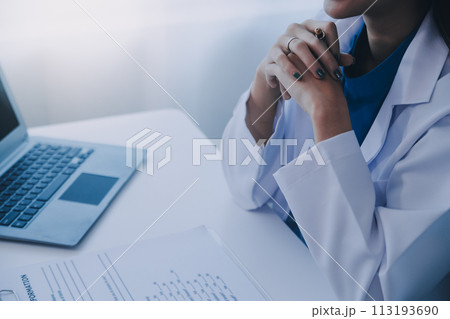 Doctor and patient sitting at the desk in clinic office. The focus is on female physician's hands filling up the medication history record form, close up. Medicine concept 113193690