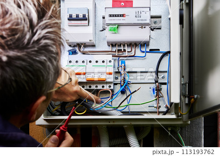 External distribution board on wood wall of rural house, installer connects power cable to load. 113193762