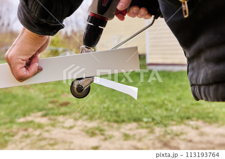 Sheet metal cutting gears are rotated by an electric drill, being adapter attachment, roofer cuts roofing steel outdoors. 113193764