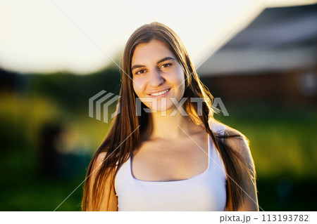 Portrait of young Caucasian woman against blurred rural background in light of setting sun in summer. Portrait of young Caucasian woman against blurred rural background in light of setting sun in summer. 113193782