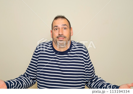 Hispanic man with beard in his 40s isolated on beige background doubting and shrugging shoulders in questioning gesture 113194334