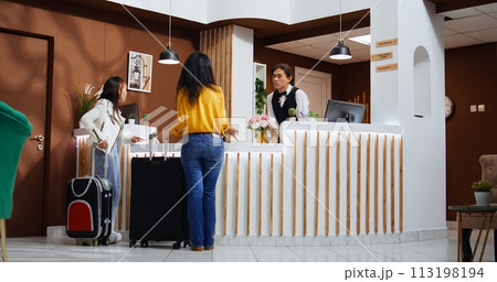 Asian tourists entering hotel lobby and using service bell, ringing to call employees and offer support at check in. Travelers requesting assistance from front desk staff, hospitality industry. Asian tourists entering hotel lobby and using service bell, ringing to call employees and offer support at check in. Travelers requesting assistance from front desk staff, hospitality industry. 113198194