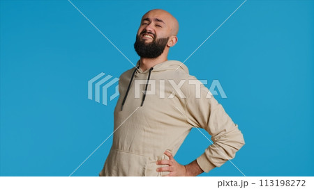 Middle eastern model dealing with lower back pain, having sore muscles because of bad posture. Arab person massaging the spine in pain to relieve discomfort in studio. Camera 1. Middle eastern model dealing with lower back pain, having sore muscles because of bad posture. Arab person massaging the spine in pain to relieve discomfort in studio. Camera 1. 113198272