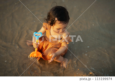 happy toddler baby girl playing toy and water on sea beach happy toddler baby girl playing toy and water on sea beach 113199974