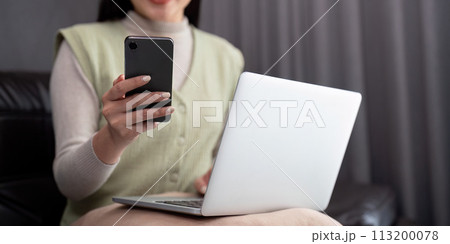 Young business woman using mobile phone, working on laptop computer at home. Female freelancer online working, using smartphone surfing the internet, remote work Young business woman using mobile phone, working on laptop computer at home. Female freelancer online working, using smartphone surfing the internet, remote work 113200078