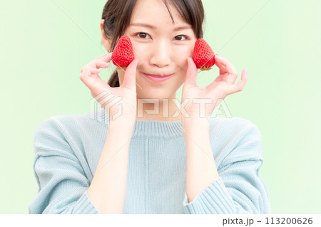 イチゴを手に持って笑顔を見せる若い女性 イチゴを手に持って笑顔を見せる若い女性 113200626