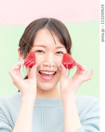 イチゴを手に持って笑顔を見せる若い女性 イチゴを手に持って笑顔を見せる若い女性 113200629
