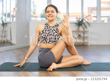 Smiling young woman performing Matsyendrasana twisting asana Smiling young woman performing Matsyendrasana twisting asana 113201744