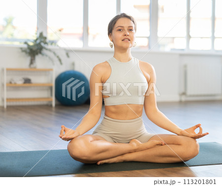 Slender girl doing hatha yoga in lotus position in bright gym Slender girl doing hatha yoga in lotus position in bright gym 113201801