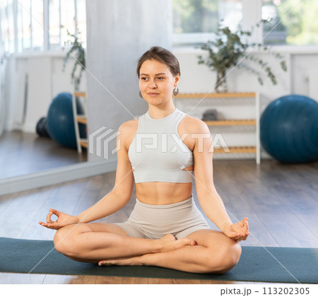 Slender girl doing hatha yoga in lotus position in bright gym 113202305