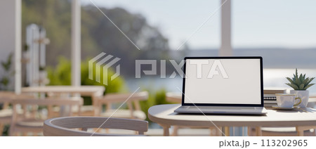 A laptop computer mockup on a table in a beautiful contemporary cafe or restaurant by the beach. 113202965
