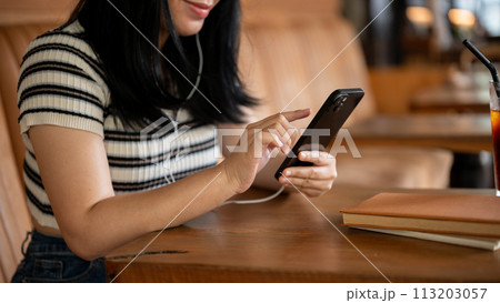 A woman sitting in a coffee shop, using her phone and listening to music on her headphones. 113203057