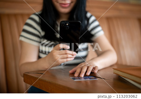 A woman registering her credit card on a shopping app on her mobile phone, sitting in a cafe. A woman registering her credit card on a shopping app on her mobile phone, sitting in a cafe. 113203062