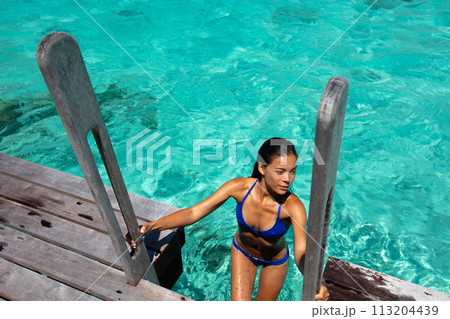 Beach travel vacation luxury woman in hotel villa swimming from ocean deck wearing bikini. This image is completely unretouched and unedited and model is with no makeup. Original Raw Image. 113204439