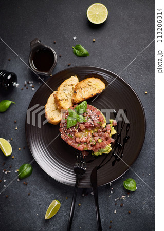 Tuna and avocado tartare with sesame seeds, capers and egg yolk on a dark ceramic plate with baguette bread crouton chips Tuna and avocado tartare with sesame seeds, capers and egg yolk on a dark ceramic plate with baguette bread crouton chips 113206314