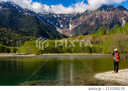 Female hiker next to a pond in front of towering, snowcapped mountains (Kamikochi, Japan) 113208210