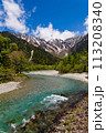 Clear, fast flowing mountain river in a forested valley in front of snowy peaks 113208340