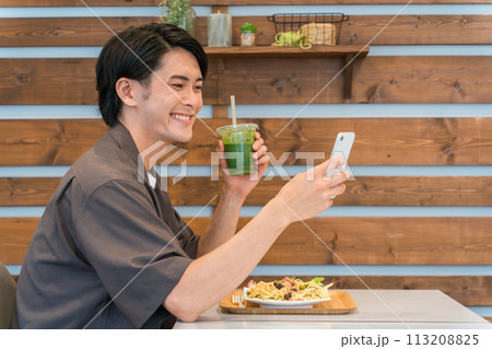 カフェでスマホを見ながらグリーンスムージーを飲む若い男性(酵素・ヘルシー・食物繊維・健康食品) カフェでスマホを見ながらグリーンスムージーを飲む若い男性(酵素・ヘルシー・食物繊維・健康食品) 113208825