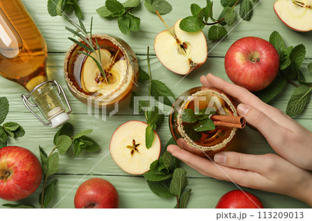 Glasses and bottle with apple cider, apples, mint and hand on green wooden background, top view 113209013