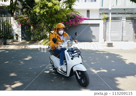 Young Vietnamese man working as courier riding motorbike Young Vietnamese man working as courier riding motorbike 113209115