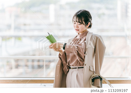 スケジュール帳を見ながら腕時計で時間を確認するビジネスウーマン・若い女性 113209197