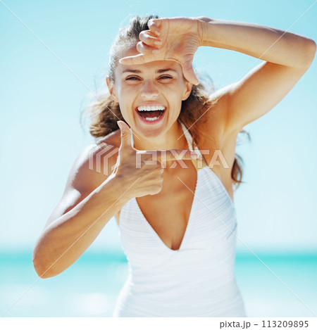 Smiling young woman framing with hands on beach 113209895
