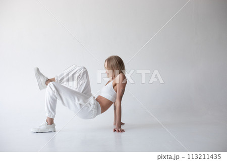 Beautiful blonde girl in a white top and tights posing on a white background Beautiful blonde girl in a white top and tights posing on a white background 113211435