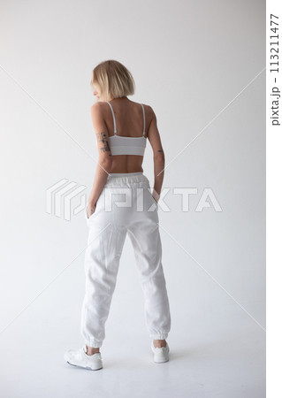 Beautiful blonde girl in a white top and tights posing on a white background. Posing with his back. Beautiful blonde girl in a white top and tights posing on a white background. Posing with his back. 113211477
