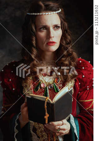pensive medieval queen in red dress with book and rosary 113211632